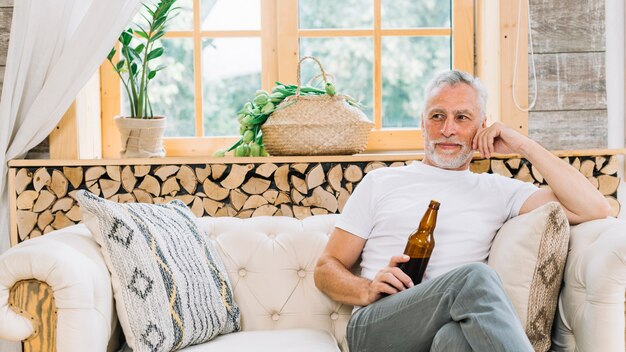 Kostenloses Foto Älterer mann des ruhestandes, der die bierflasche sitzt auf sofa hält