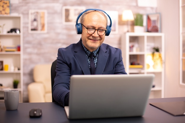 Kostenloses Foto Älterer mann in den 60ern mit kopfhörern auf dem kopf, der musik hört und an einem modernen laptop arbeitet