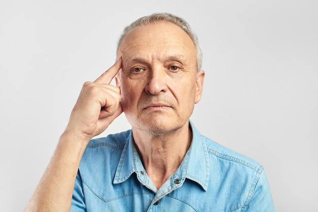 Älterer mann zeigt mit dem finger auf seinen kopf auf weißem hintergrund. alterskrankheiten, demenz, alzheimer, schlechtes gedächtniskonzept