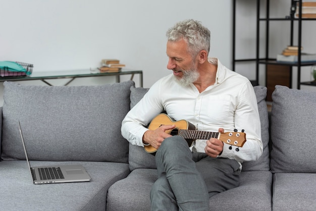 Kostenloses Foto Älterer mann zu hause, der ukulele-unterricht auf dem laptop studiert