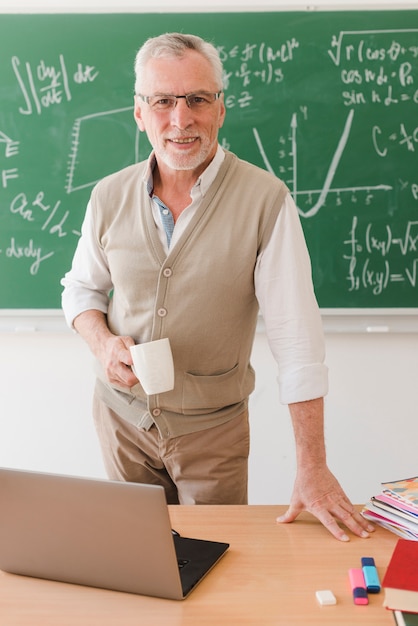 Kostenloses Foto Älterer professor, der hinter schreibtisch im klassenzimmer steht