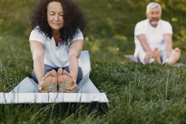 Kostenloses Foto Älteres paar macht yoga im freien. dehnen im park während des sonnenaufgangs. brünette in einem weißen t-shirt.