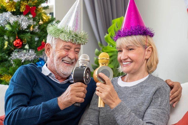 Kostenloses Foto Älteres paar mann und frau singen lied weihnachtslied zusammen sitzen auf sofa mit baum und dekoration im hintergrund