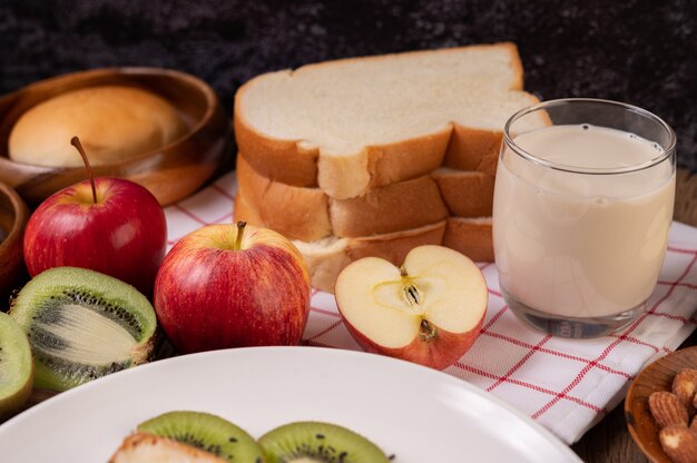 Äpfel, kiwi, milch und brot in einem teller auf einem rotweißen tuch