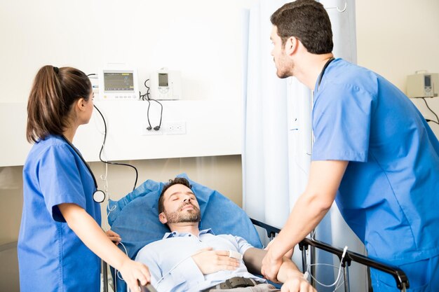 Ärzteteam untersucht den Blutdruck eines Patienten und betrachtet den Herzfrequenzmonitor. Patient liegt im Bett in der Notaufnahme.