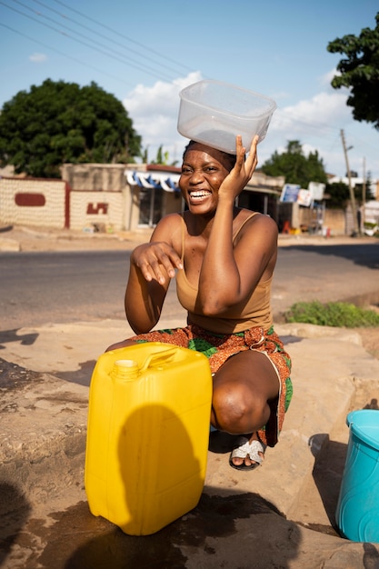 Afrikanerin gießt wasser in einen empfänger im freien