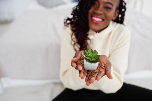 Afrikanerin im Hoodie hält kleinen Blumentopf zu Hause