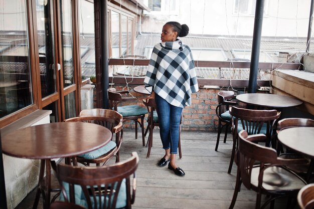 Afrikanerin im karierten Umhang posierte auf der Terrasse des Cafés im Freien