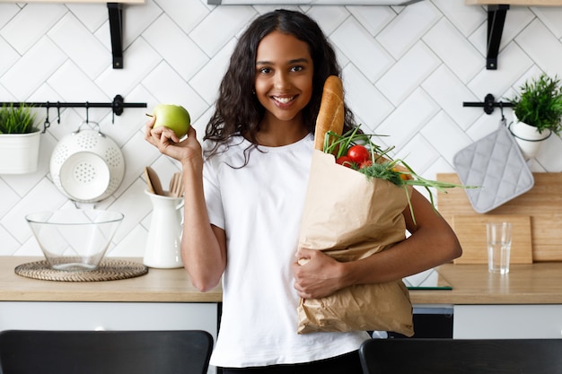 Afrikanerin steht in der Küche und hält eine Papiertüte mit Lebensmitteln