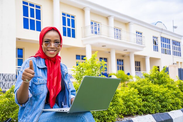 Afrikanische Frau, die das gleiche Zeichen gestikuliert, während sie mit ihrem Laptop im Park sitzt