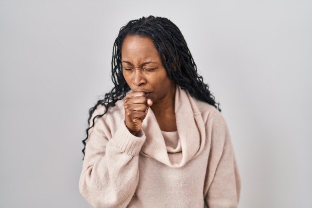 Afrikanische Frau, die vor weißem Hintergrund steht und sich unwohl fühlt und als Symptom für Erkältung oder Bronchitis hustet. Gesundheitskonzept.