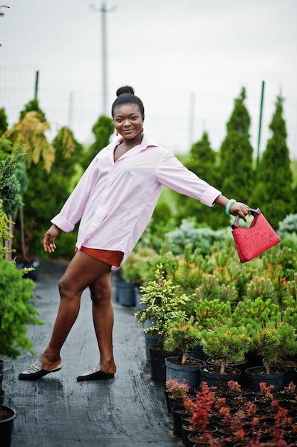 Afrikanische Frau in rosafarbenem, großem Hemd posierte im Garten mit Setzlingen