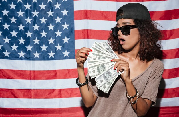 Afrikanische junge Frau mit Geld, das über USA-Flagge steht