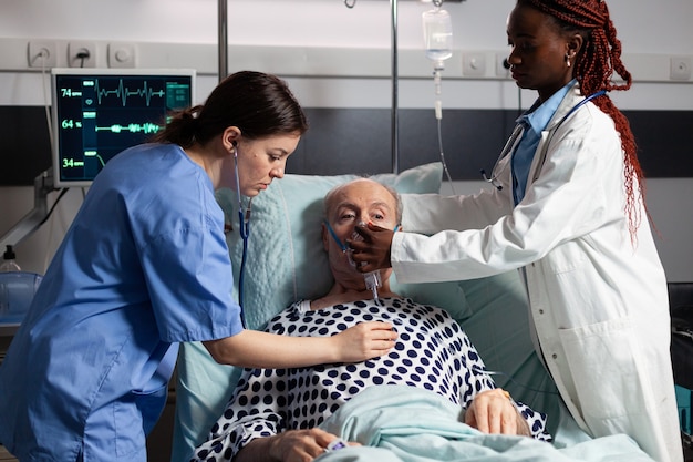 Afrikanischer Arzt und medizinischer Assistent helfen Senioren beim Atmen mit Sauerstoffmaske, im Krankenhaus im Bett liegend laying