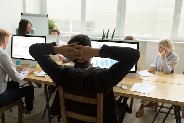 Afrikanischer Geschäftsmann, der Statistikdaten im gemischtrassigen Büro, hintere Ansicht analysiert