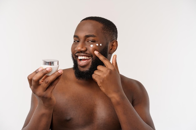 Afrikanischer gutaussehender Mann, der Creme auf sein Gesicht aufträgt, bemannt Hautpflegekonzept