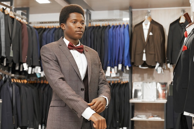 Afrikanischer Mann, der eleganten Anzug in modischer Boutique wählt.