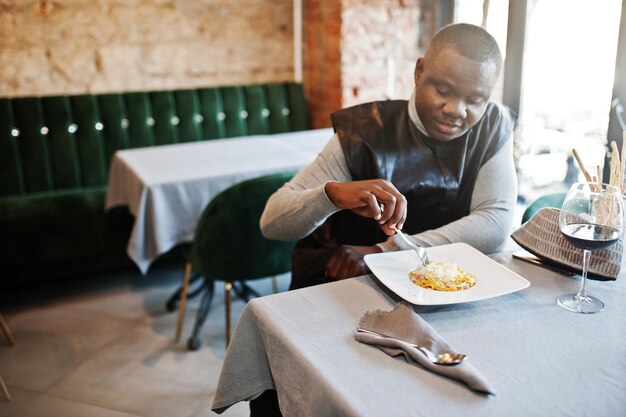 Afrikanischer Mann in schwarzer traditioneller Kleidung sitzt im Restaurant und isst Pasta