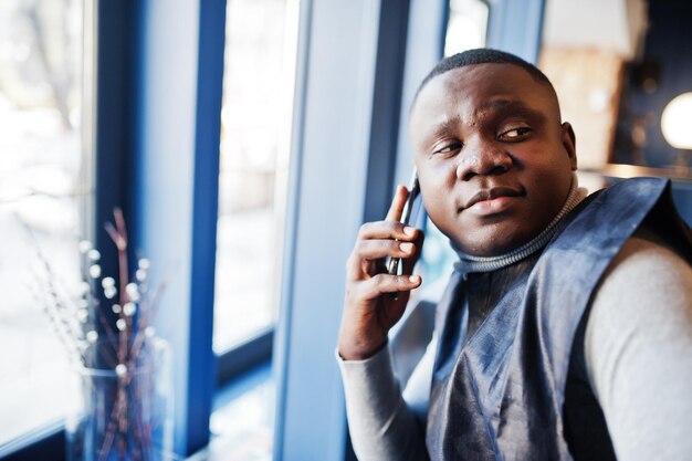 Afrikanischer Mann in schwarzer traditioneller Kleidung sitzt im Restaurant und spricht auf dem Smartphone