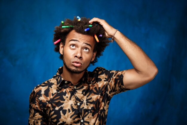 Afrikanischer Mann mit Markierungen im Haar, die über blaue Wand denken.