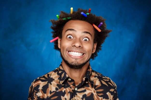 Afrikanischer Mann mit Markierungen im Haar, die über blaue Wand lächeln.