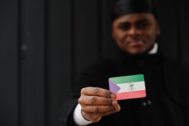 Afrikanischer Mann trägt schwarzen Durag, hält die Flagge Äquatorialguineas zur Hand, isoliert auf dunklem Hintergrund