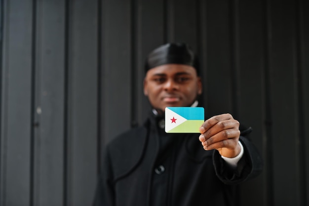 Kostenloses Foto afrikanischer mann trägt schwarzen durag, hält dschibuti-flagge zur hand, isoliert auf dunklem hintergrund