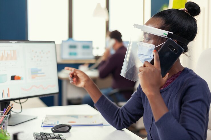 Kostenlose Foto afrikanischer mitarbeiter, der im büro auf dem smartphone spricht und eine gesichtsmaske gegen coronavirus trägt