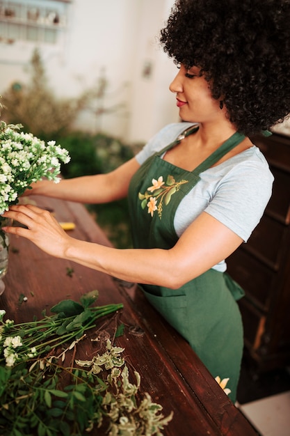 Afrikanischer weiblicher Florist, der Bündel weiße Blumen im Vase vereinbart