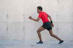 Kostenloses Foto afro athletischer mann, der draußen auf der straße läuft und übung macht