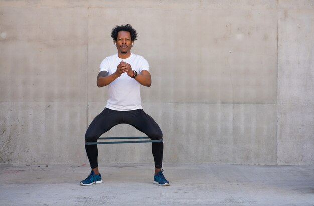 Afro athletischer Mann, der hockendes Bein im Freien ausübt und tut. Sport und gesunder Lebensstil Konzept.
