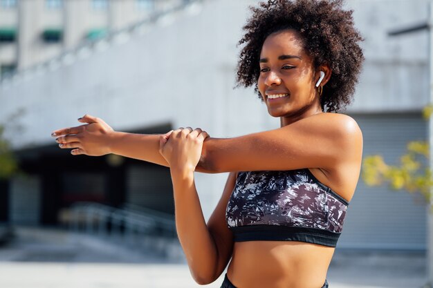 Afro sportliche Frau, die ihre Arme streckt und sich vor dem Training im Freien aufwärmt