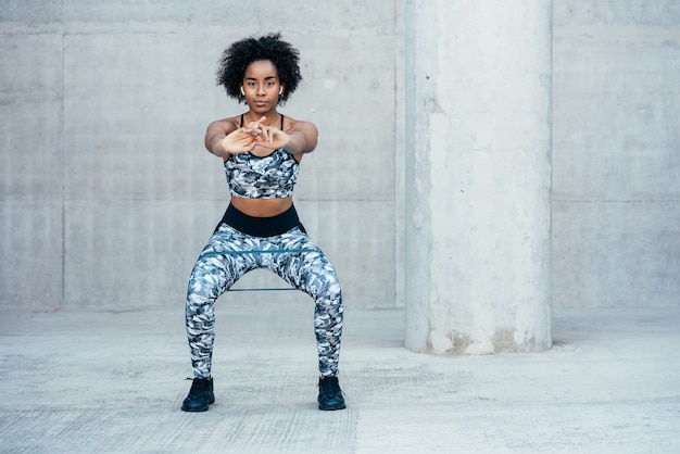 Afro sportliche Frau, die im Freien hockendes Bein ausübt und tut.