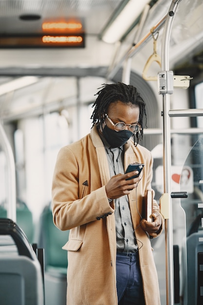 Afroamerikaner, der im Stadtbus reitet. Mann in einem braunen Mantel. Corona-Virus-Konzept.