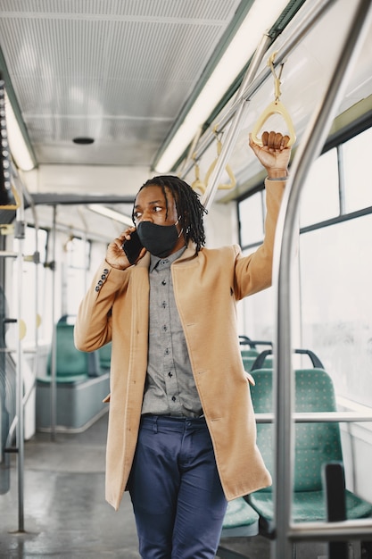 Afroamerikaner, der im Stadtbus reitet. Mann in einem braunen Mantel. Corona-Virus-Konzept.