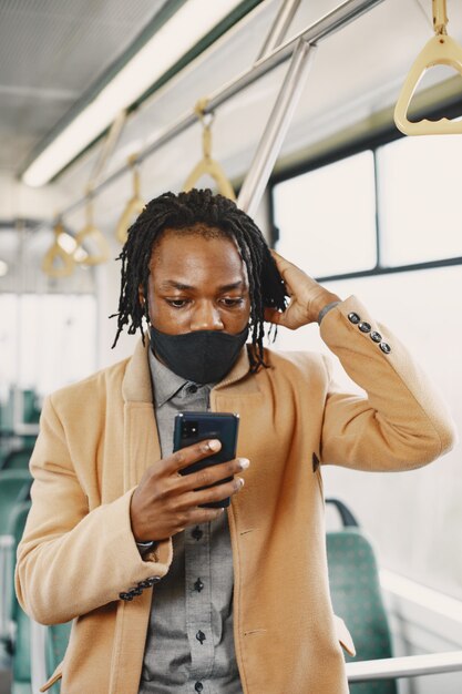 Afroamerikaner, der im Stadtbus reitet. Mann in einem braunen Mantel. Corona-Virus-Konzept.