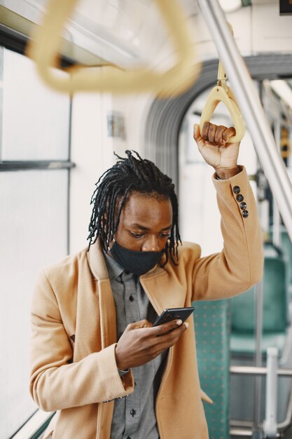 Afroamerikaner, der im Stadtbus reitet. Mann in einem braunen Mantel. Corona-Virus-Konzept.