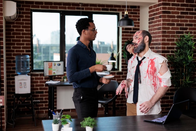 Afroamerikaner, der mit zombie im geschäftsbüro spricht, untoter, gruseliger leichnam, der mit person am startup-arbeitsplatz plaudert. böses horror-makaber-monster mit blutigen narben und verfallen.