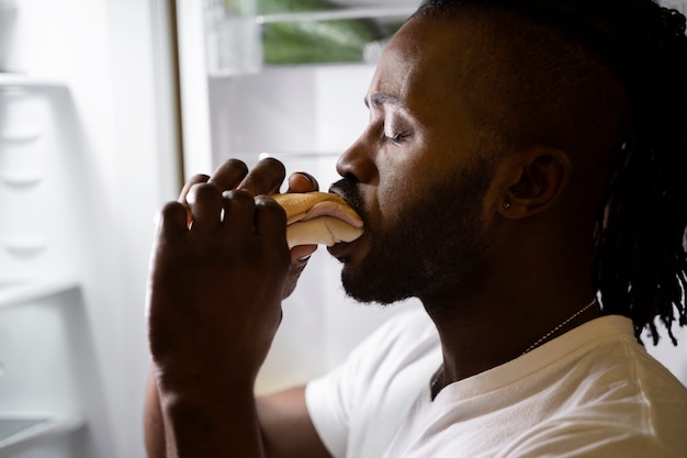 Kostenloses Foto afroamerikaner, der nachts aus dem kühlschrank isst