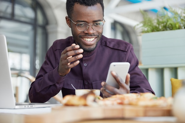 Afroamerikaner männlich in formeller Kleidung, teilt Multimedia-Dateien in Nachricht, gibt Feedback, organisiert Zeitplan