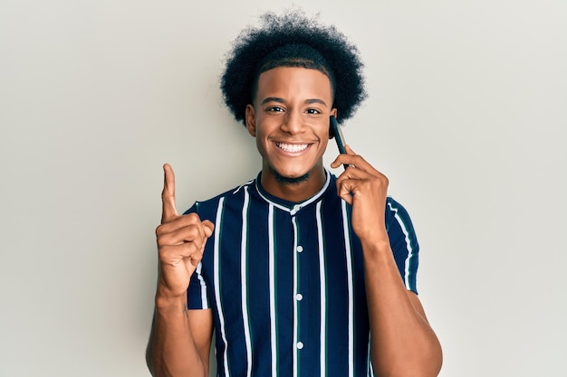 Kostenloses Foto afroamerikaner mit afro-haaren, der sich auf dem smartphone unterhält und mit einer idee oder frage lächelt und mit dem finger mit glücklichem gesicht zeigt, nummer eins