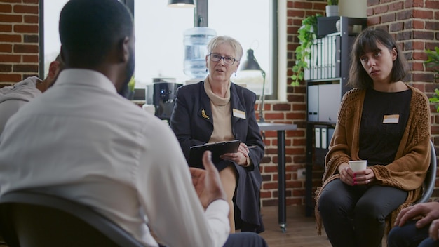 Afroamerikaner spricht mit Berater über Sucht bei einem Therapietreffen. Erwachsene, die an Selbsthilfegruppensitzungen mit Patienten und Therapeuten teilnehmen, um Alkoholismus und Depressionen zu heilen.