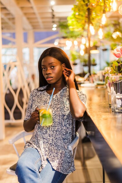 Afroamerikanerfrau, die Cocktaillimonade im Café an der Bar trinkt.