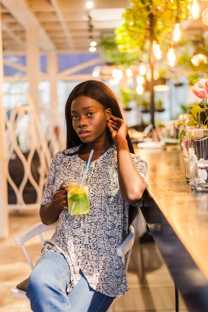 Afroamerikanerfrau, die Cocktaillimonade im Café an der Bar trinkt.