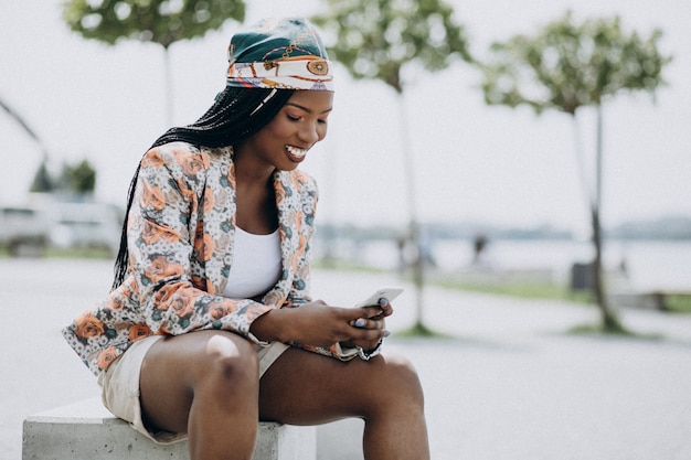 Afroamerikanerfrau, die im Park sitzt und Telefon verwendet