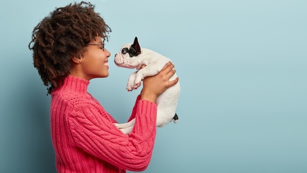 Afroamerikanerfrau, die rosa Pullover hält Hund hält