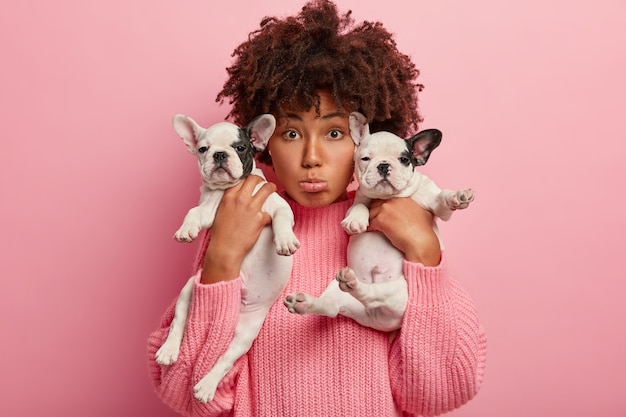 Afroamerikanerfrau, die rosa Pullover hält Welpen hält