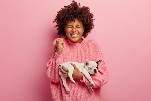 Afroamerikanerfrau, die rosa Pullover hält Welpen hält