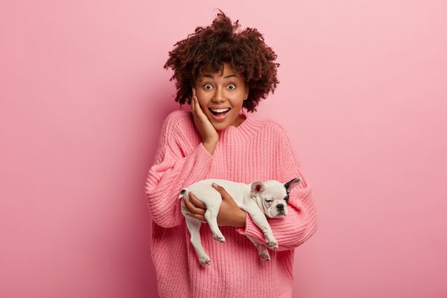 Afroamerikanerfrau, die rosa Pullover hält Welpen hält