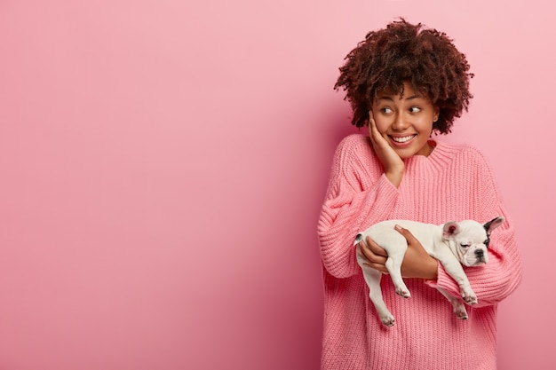 Afroamerikanerfrau, die rosa Pullover hält Welpen hält